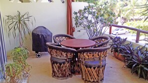 A patio with a round table and chairs, surrounded by potted plants and a barbecue grill.
