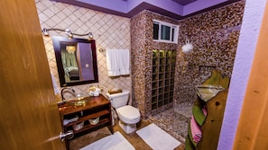 A bathroom with a glass sink, a toilet, a shower with a mosaic wall, and a wooden vanity.