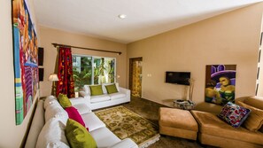 A living room with a white sofa, a tan sofa, and a coffee table. There is a TV on the wall and a painting on the wall.