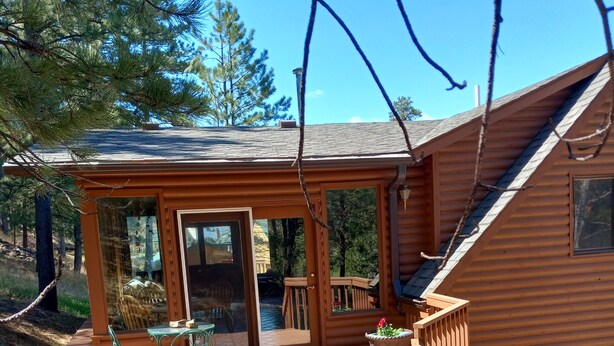A wooden cabin with a covered patio, outdoor seating, and a small garden area. - In town home- above the 1880 train.  Walk to Main St!— recently updated! (Hill City)