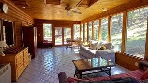 A spacious wooden cabin with a high ceiling, large windows, a ceiling fan, and a cozy seating area with a sofa and armchair. - In town home- above the 1880 train.  Walk to Main St!— recently updated! (Hill City)