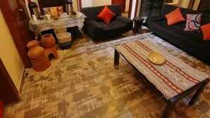 A living room with a patterned rug, two sofas with orange cushions, a coffee table with a woven placemat, and a door with a wooden frame. - Casona Quera (Cusco)