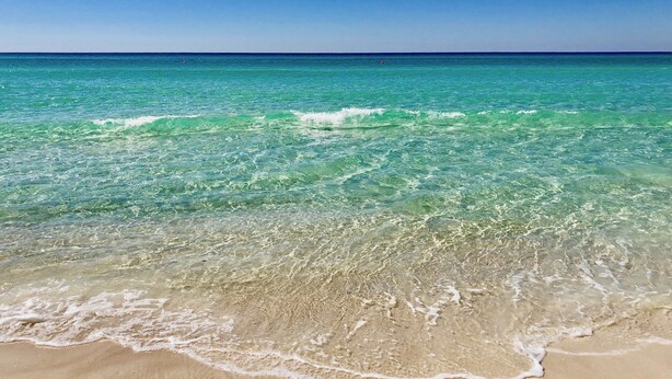 Une plage à l’eau turquoise et limpide, où les vagues sont douces.