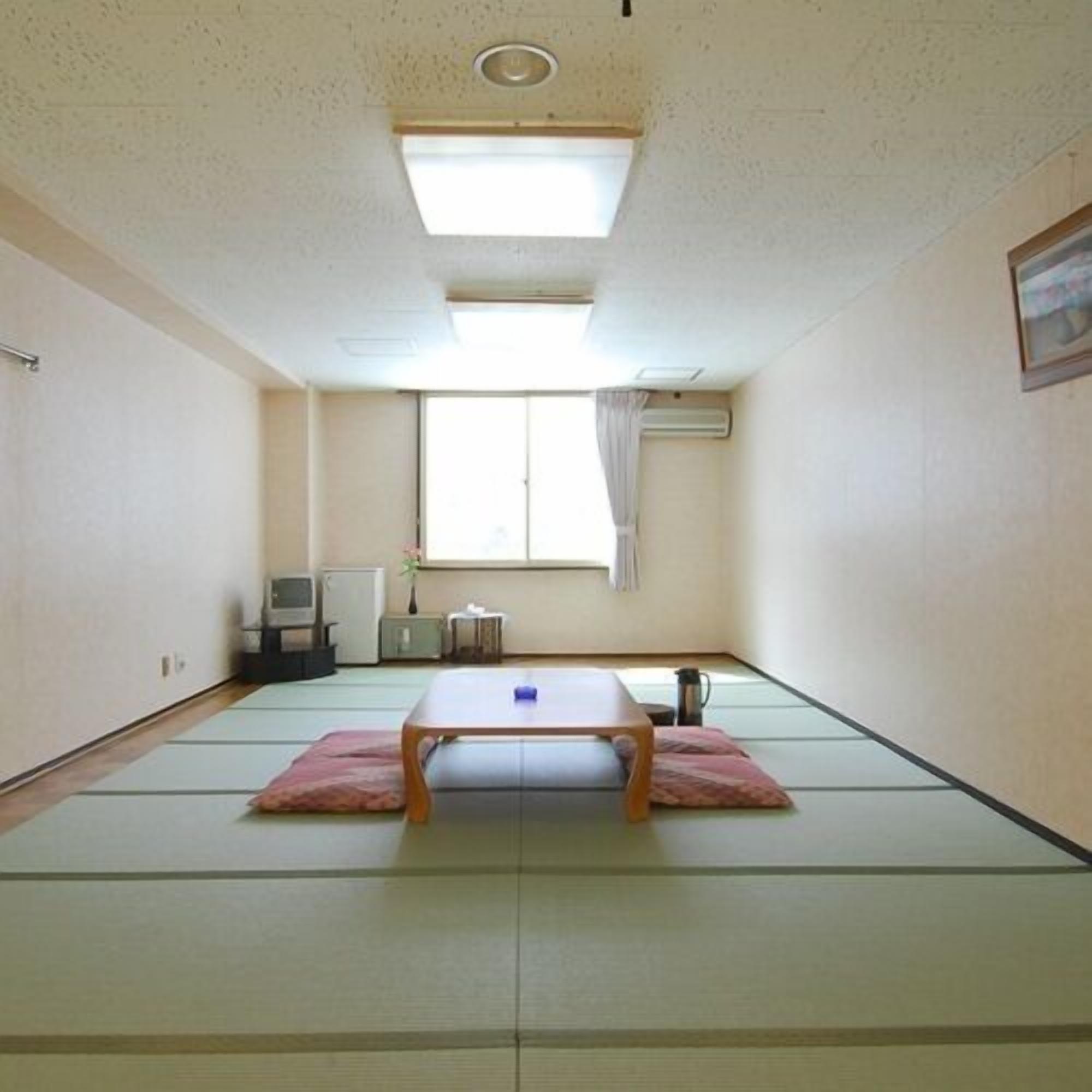 A room with tatami mats, a low table, a TV, a radiator, and a window with curtains.