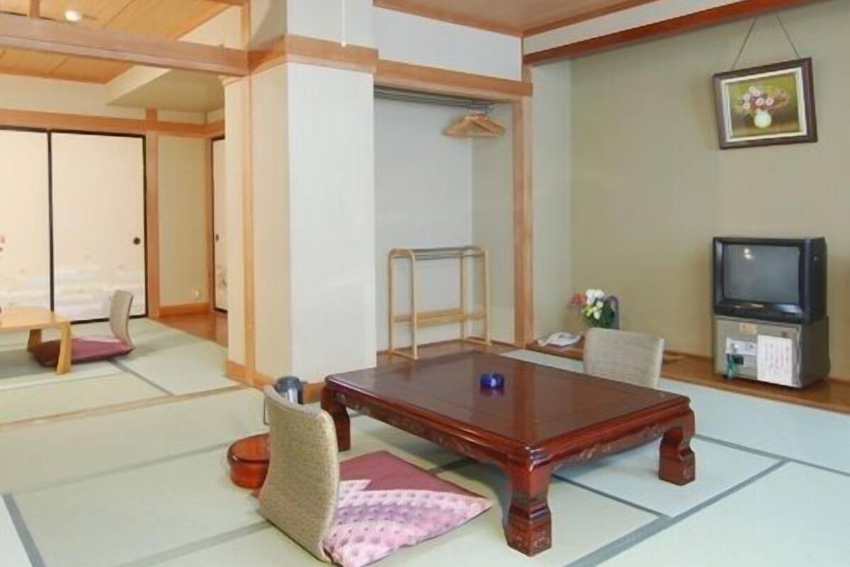 A traditional Japanese room with tatami flooring, a low wooden table, a television, and a sliding door.
