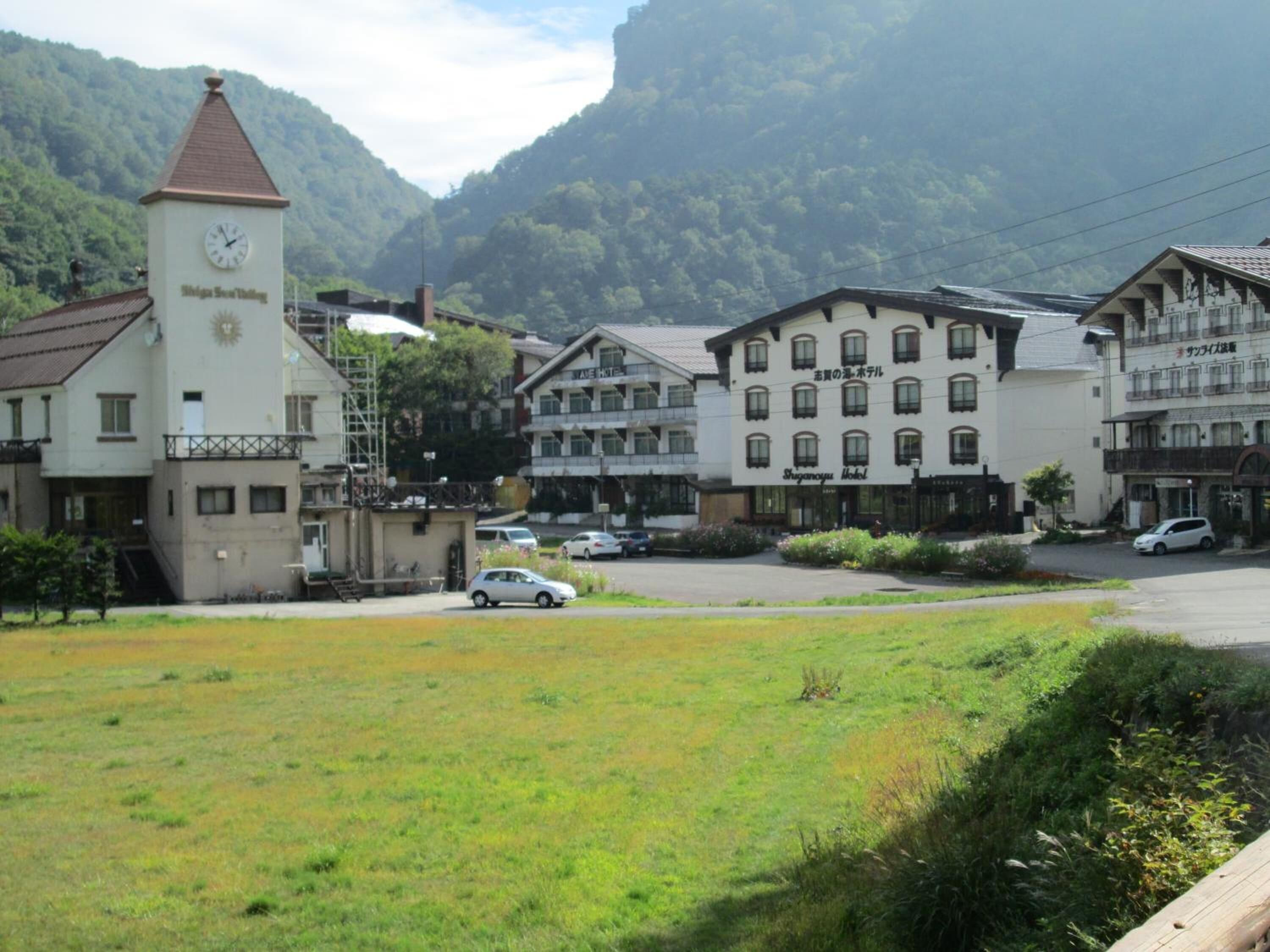 A hotel with a clock tower, surrounded by lush greenery and mountains.