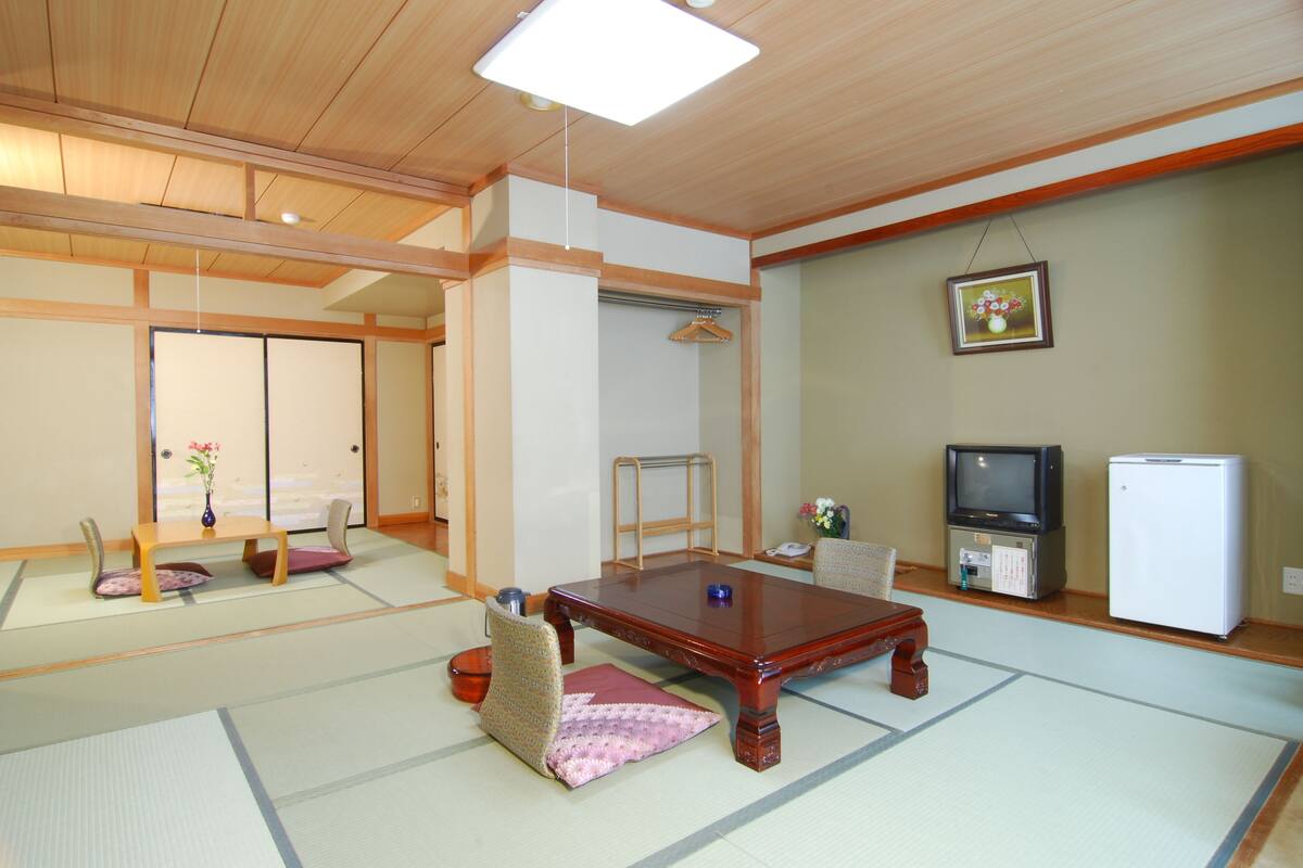 A traditional Japanese room with tatami flooring, a low wooden table, a television, and a refrigerator.