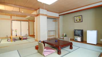 A traditional Japanese room with tatami flooring, a low wooden table, a television, and a refrigerator.