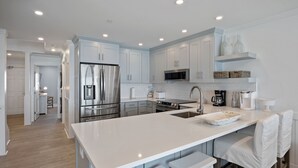 A modern kitchen with white cabinetry, stainless steel appliances, and a large island with bar stools. - Splash in the water, play in the sand, REJUVENATE! 205- Destin Seafarer (Destin)