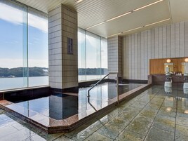 Una piscina interior moderna con vistas a un lago, una recepción de madera y una pared con azulejos.