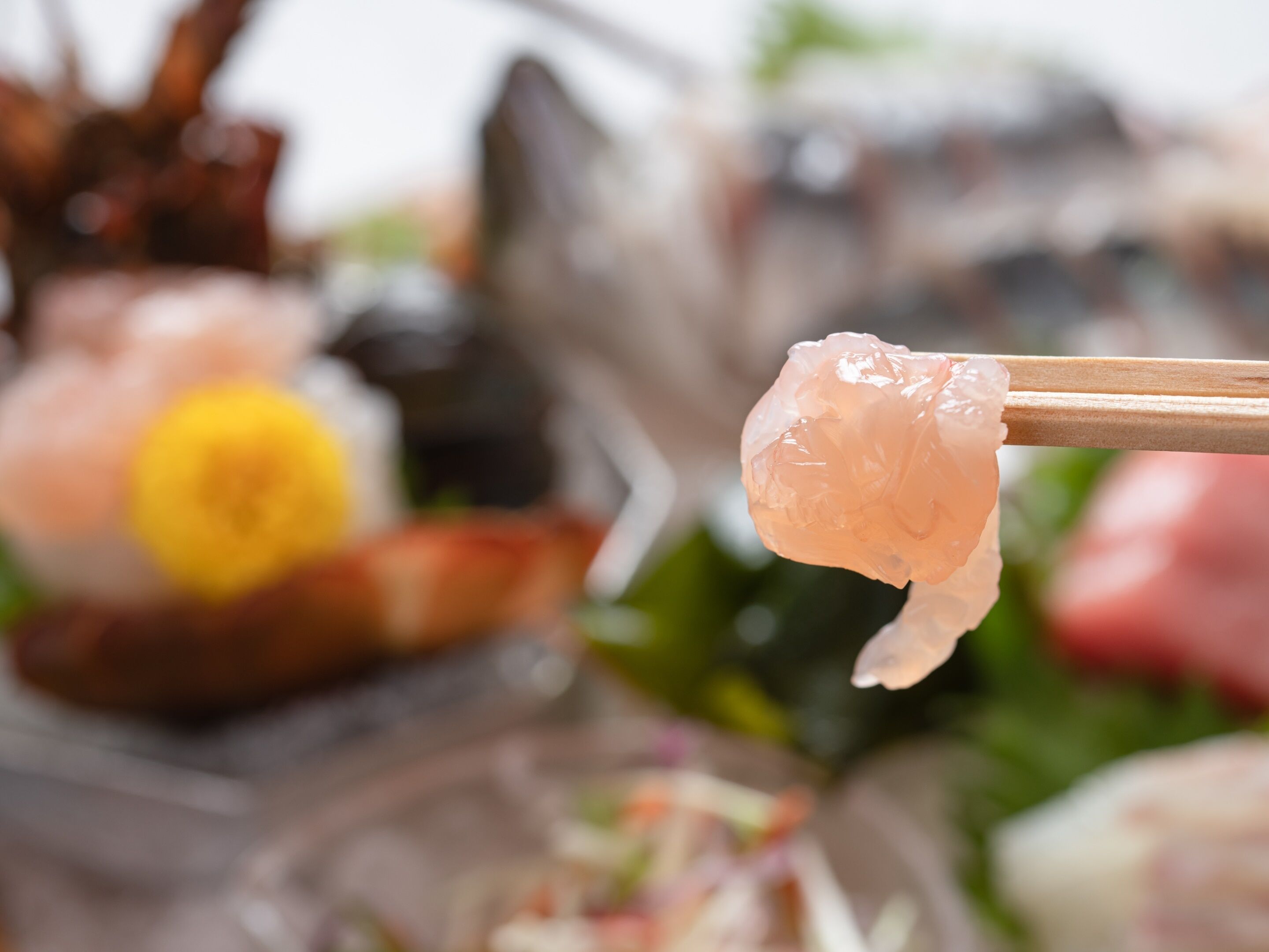Close-up de uma peça de sushi segurada com hashis, com outras peças de sushi desfocadas ao fundo.
