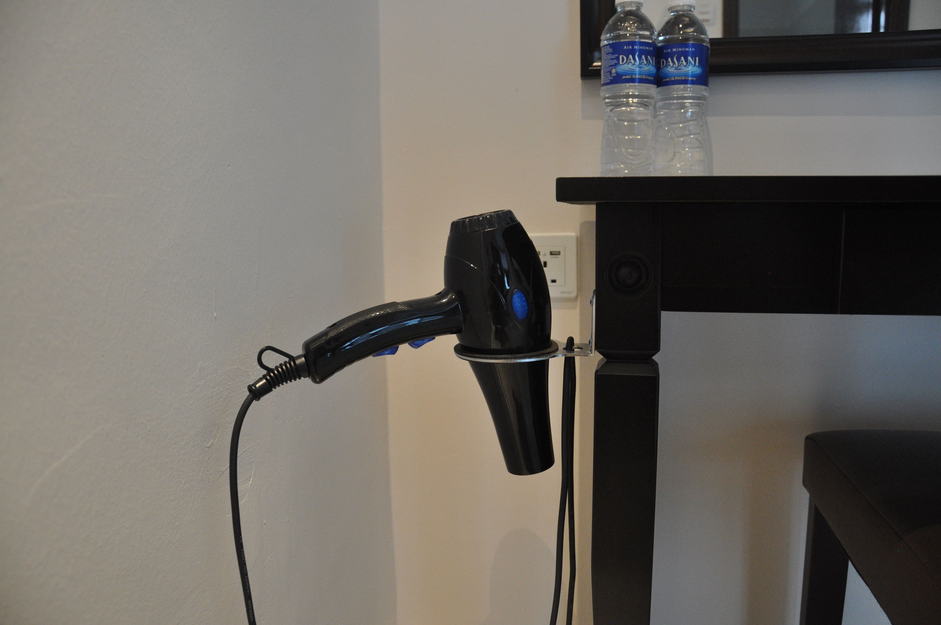Un secador de pelo conectado a un enchufe de pared, una mesa negra y dos botellas de agua encima de la mesa.
