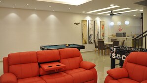 A modern living room with a pool table, red sofas, and a foosball table.