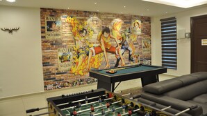 A room with a pool table, a foosball table, and a brick-patterned wall with 'Wanted' posters.