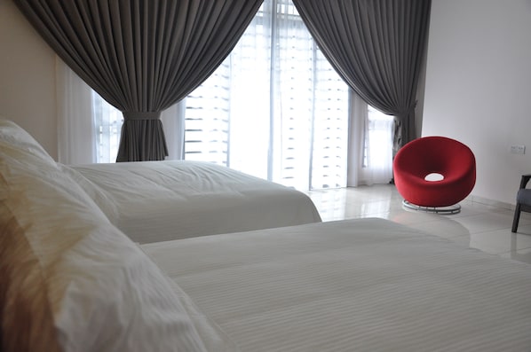 A hotel room with two beds, a red chair, and a view of a building through large windows.