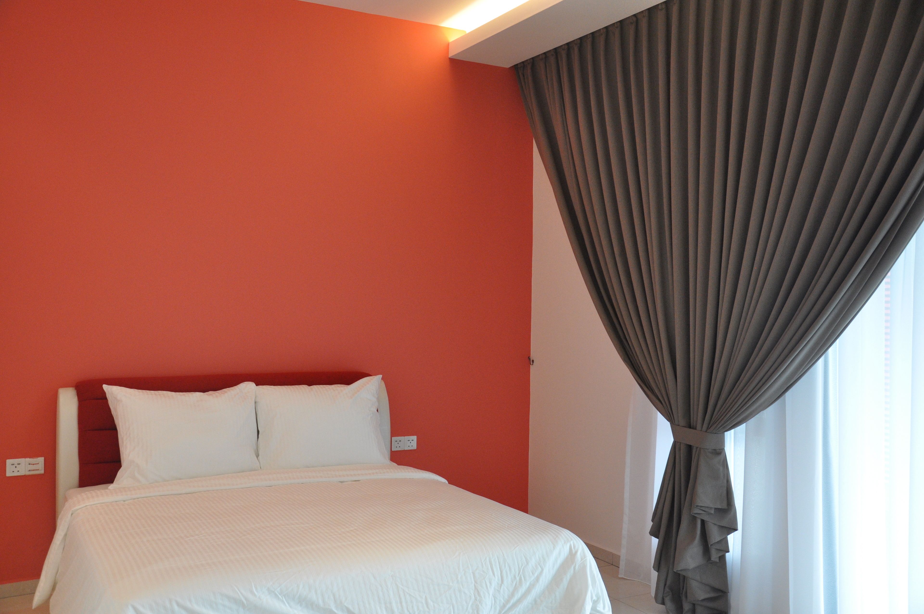 A hotel room with a bed, a red wall, and a grey curtain.