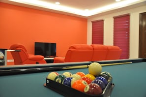 A pool table with balls, a television, and orange chairs in a room with orange walls.