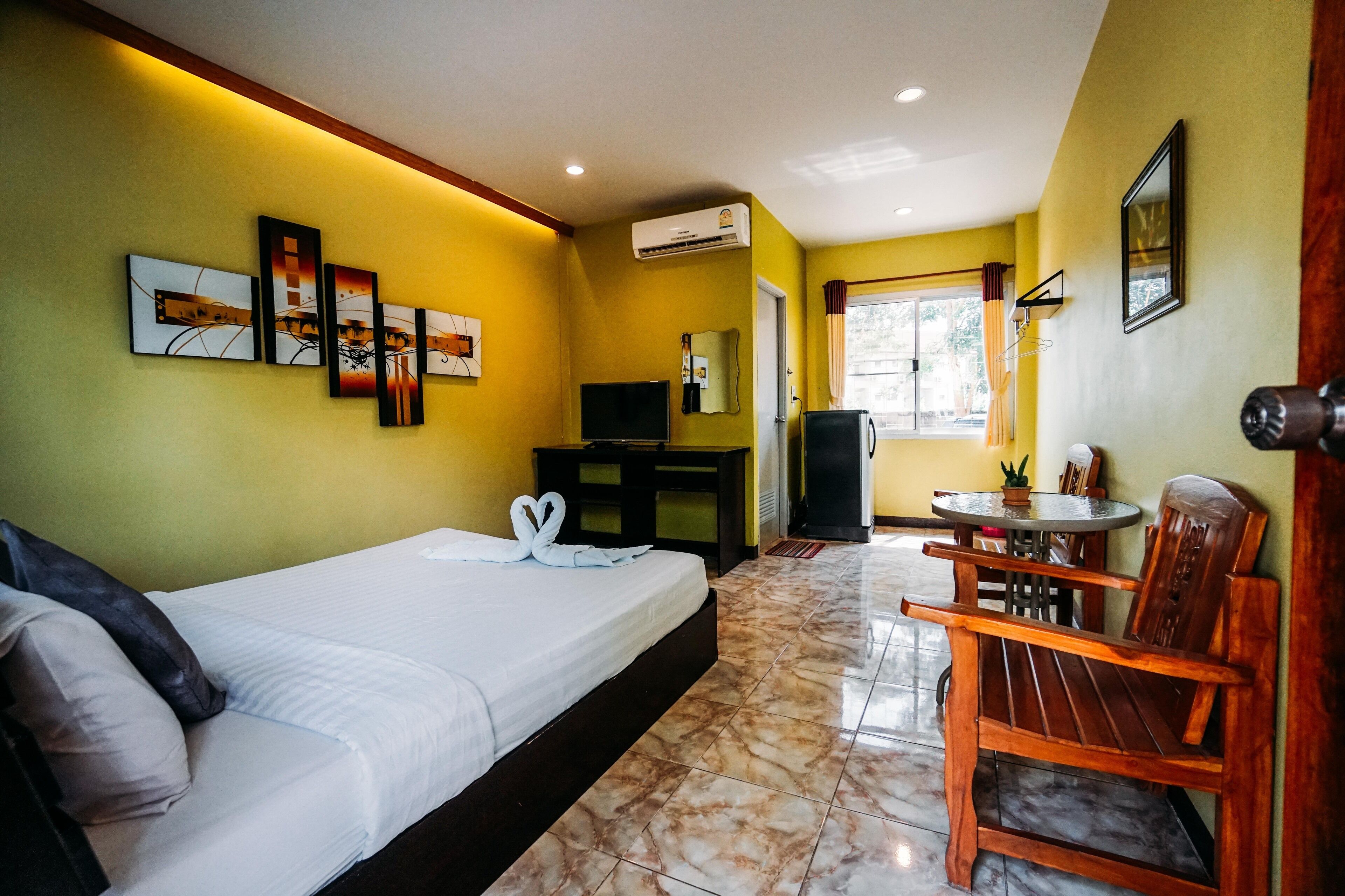 A hotel room with a bed, a desk, a chair, a TV, and artwork on the wall.