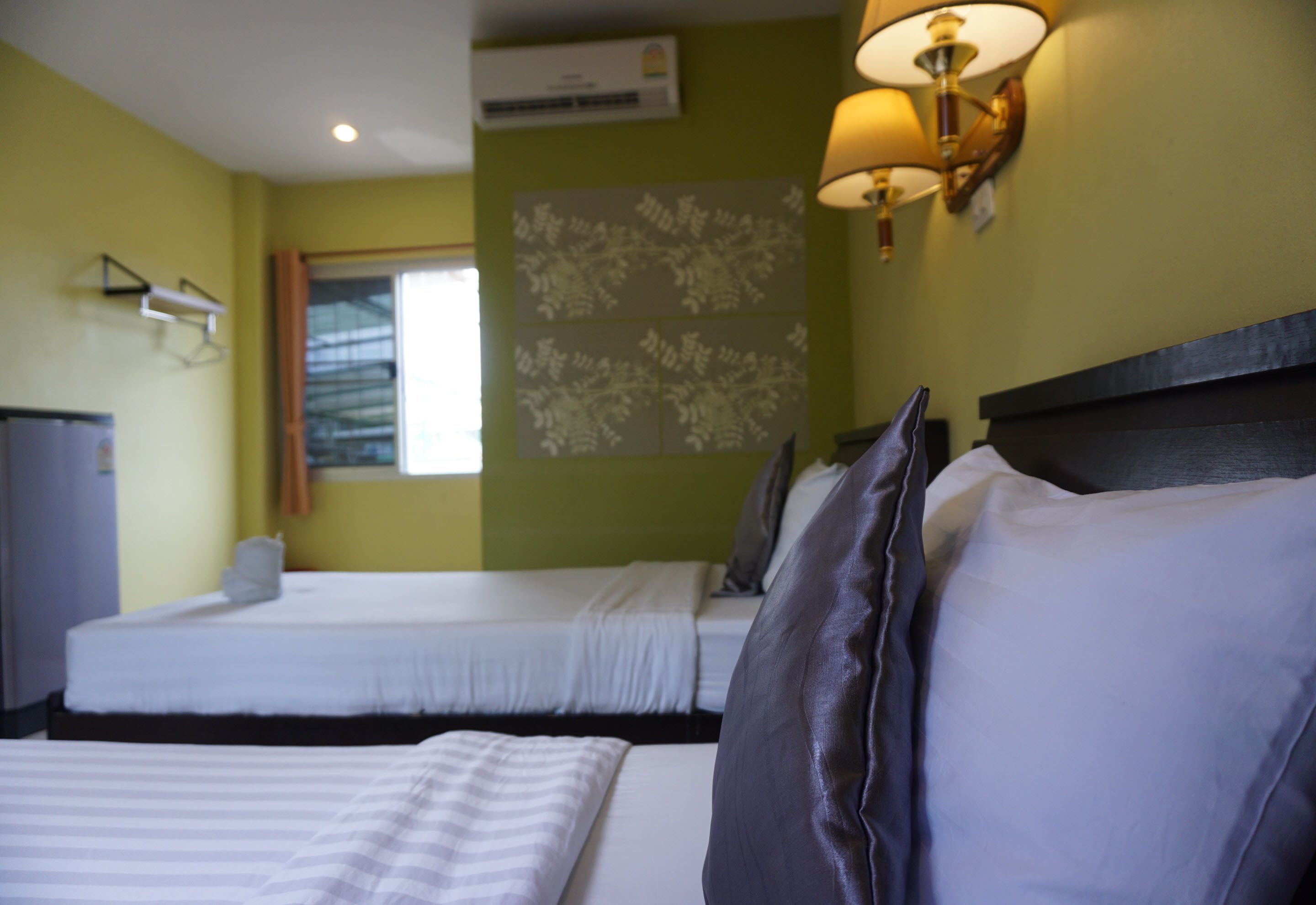 A hotel room with two beds, a window, a wall-mounted air conditioner, and a lamp.