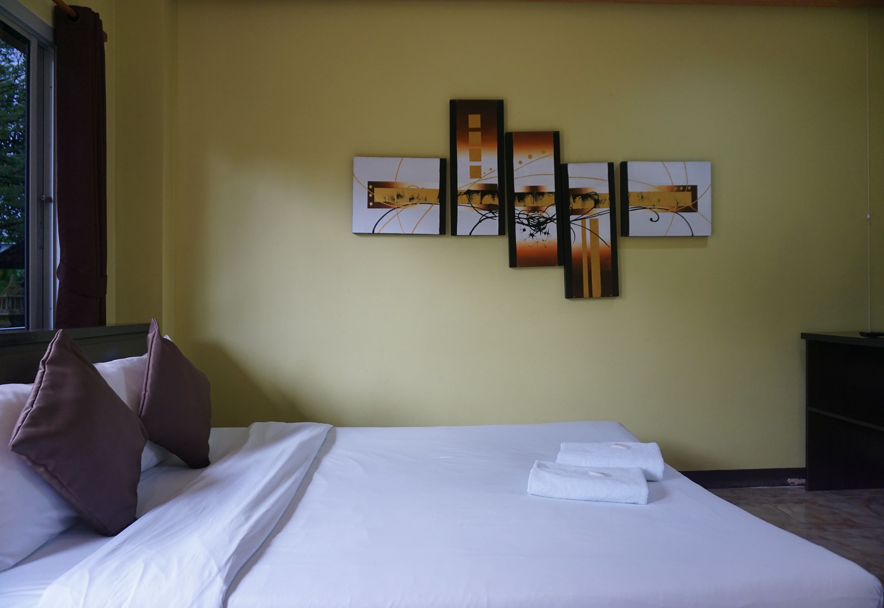 A hotel room with a bed, pillows, a wall-mounted artwork, and a nightstand.