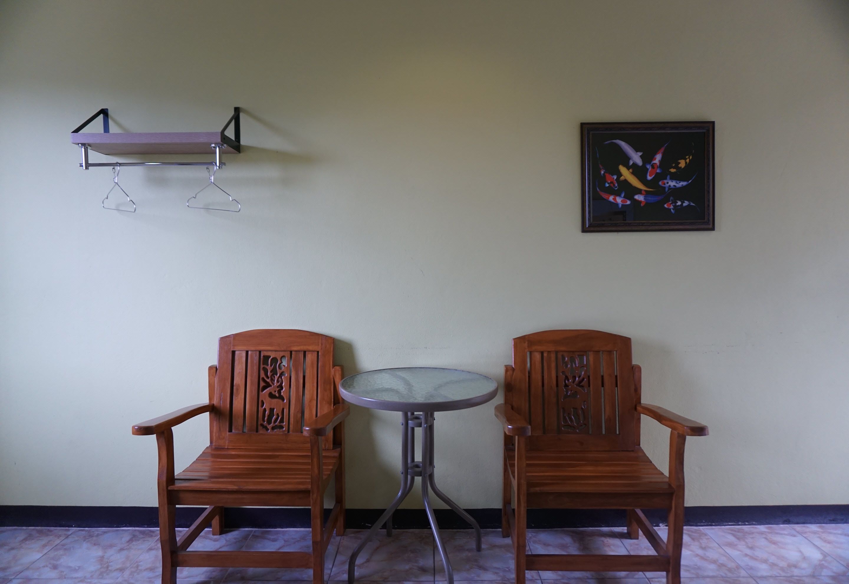 Dos sillas de madera con intrincados grabados, una pequeña mesa redonda, un estante sujeto a la pared y un cuadro con peces.