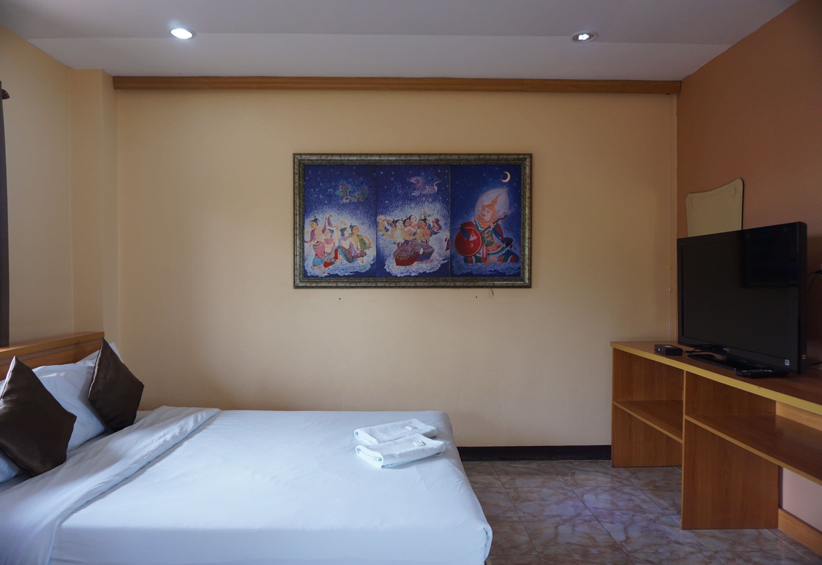 A hotel room with a bed, a painting on the wall, a television, and a wooden desk.
