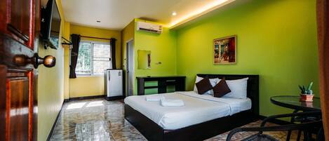 Una habitación de hotel con cama, escritorio, silla, una mesita con planta en maceta y un equipo de aire acondicionado.