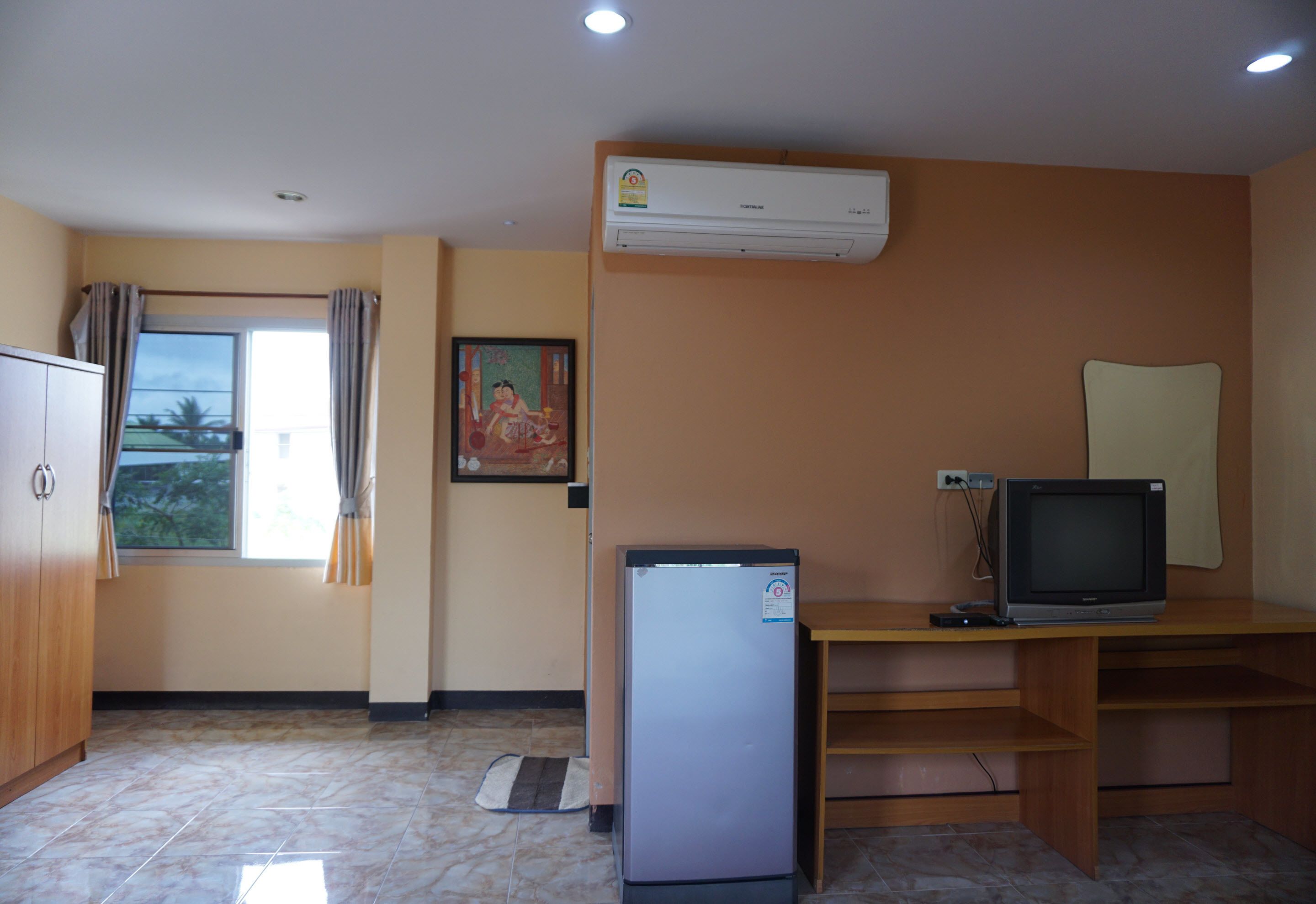Una habitación pequeña con refrigerador, televisor y ventana con cortinas.