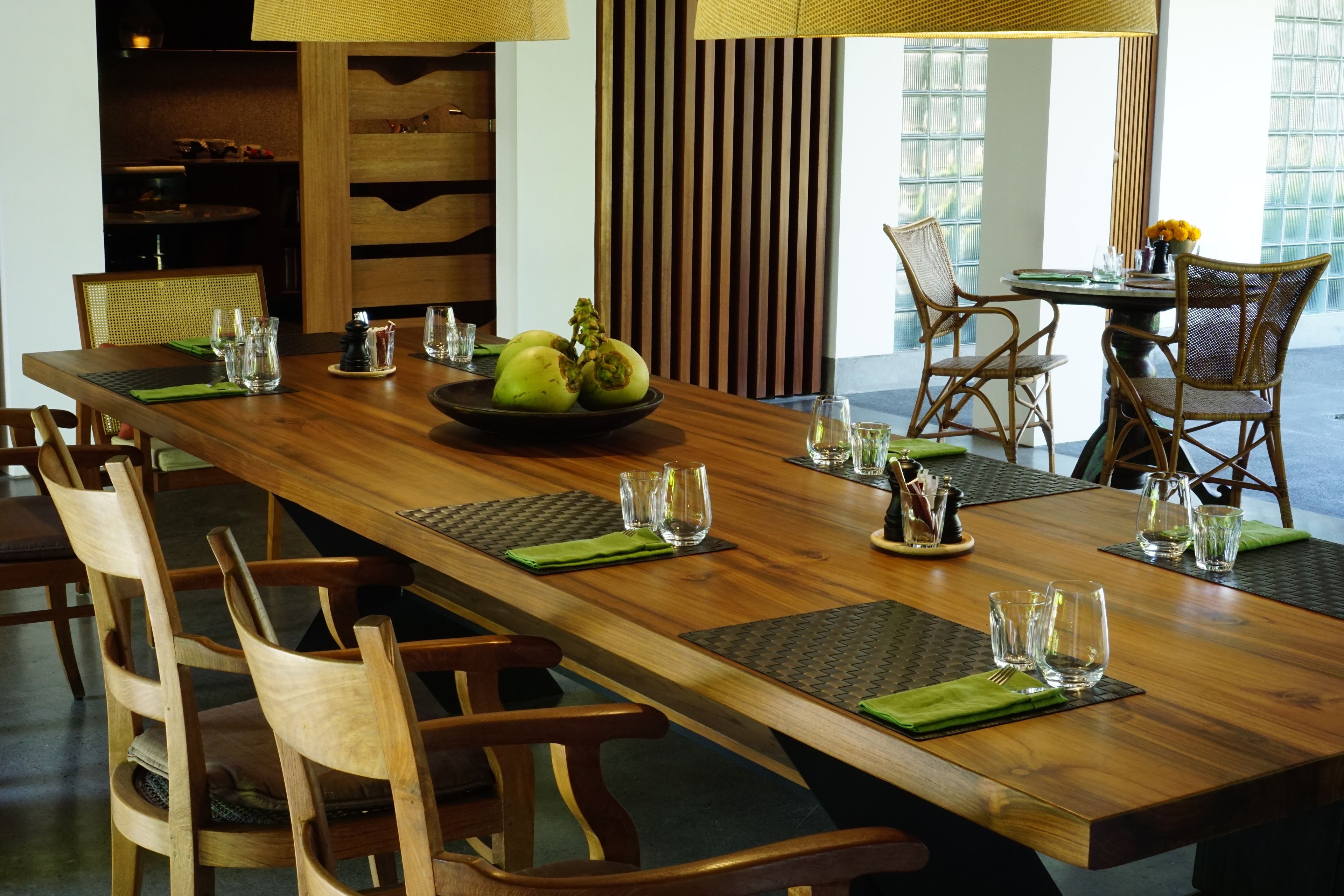 A long wooden dining table with chairs, set with glassware and a bowl of fruit.