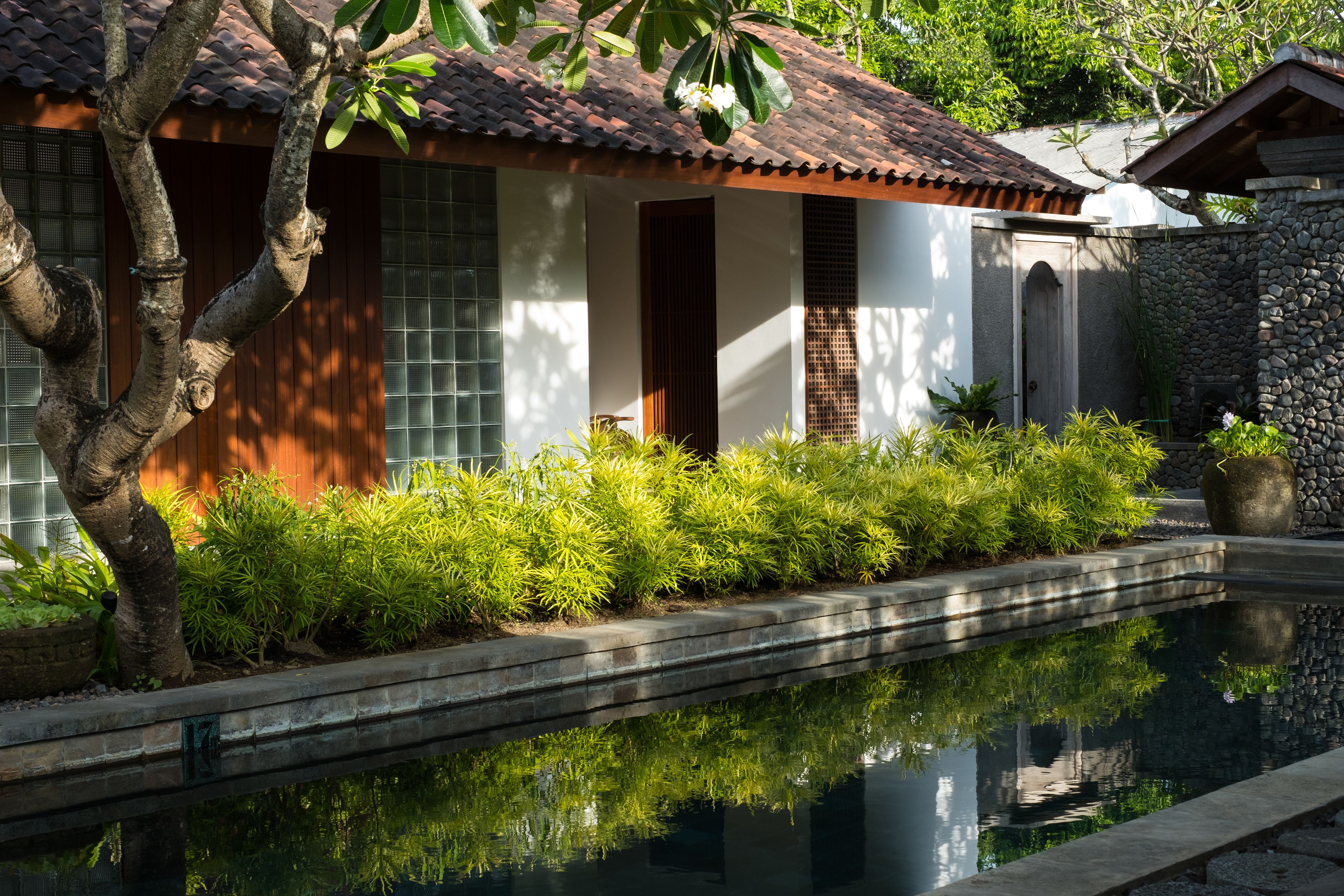 A traditional house with a tiled roof, a stone wall, and a small pool reflecting the surroundings.