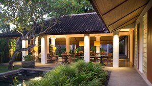 A covered outdoor dining area with tables and chairs, surrounded by lush greenery and a small water feature. - Atelier TE Designer Guesthouse (Denpasar)