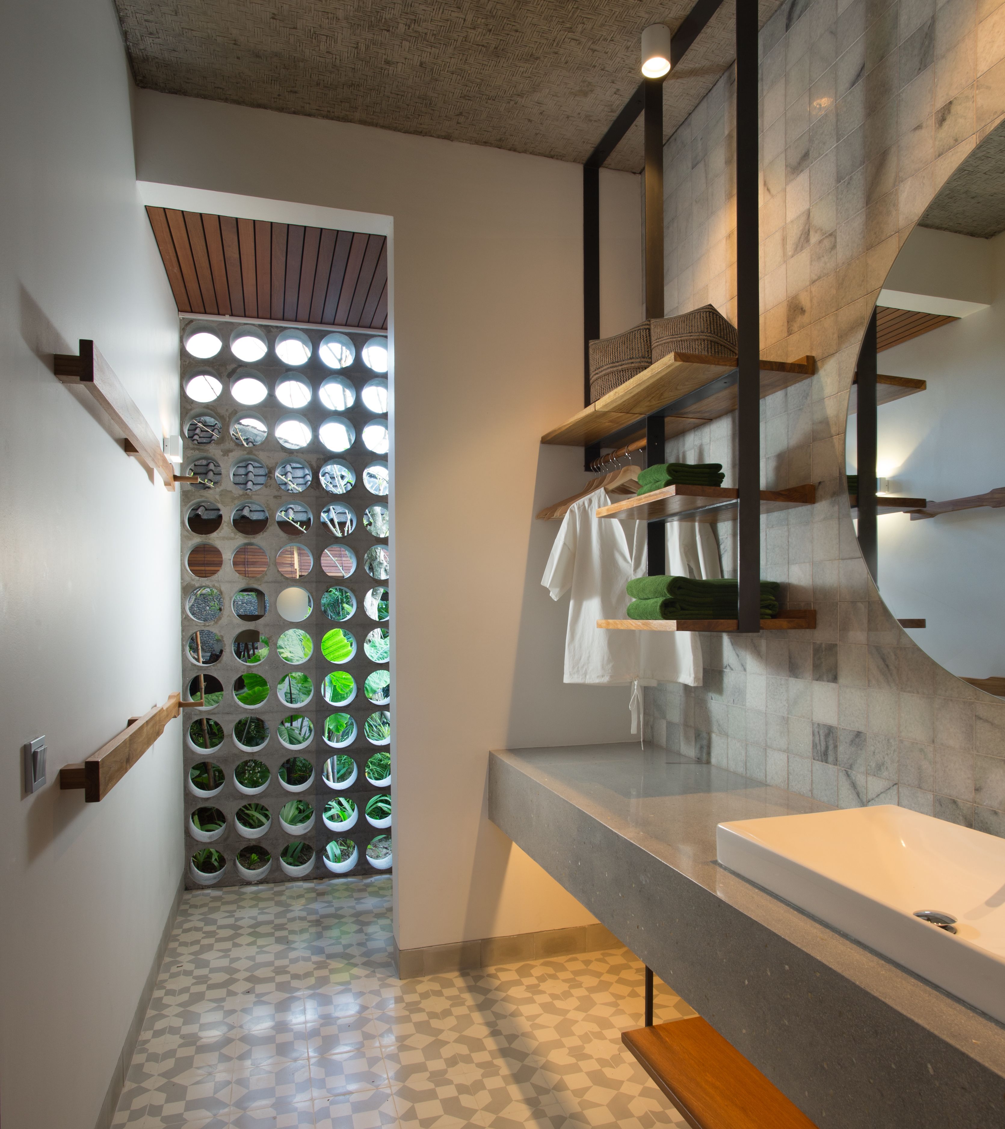 A modern bathroom with a geometric tile floor, a built-in planter wall with circular windows, and a minimalist design with wooden shelves and a large mirror.