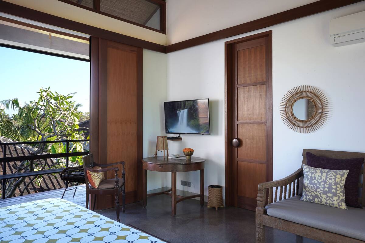 Une chambre avec un lit, une chaise en bois, une petite table avec un téléviseur et une vue sur les arbres.