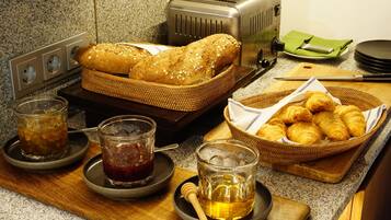Une table dressée pour le petit-déjeuner avec du pain, des croissants, du miel et des boissons fraîches, le tout disposé sur une planche en bois.