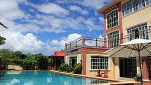 Zona de piscina con cielo azul despejado, un edificio de techo rojo y una sombrilla blanca.