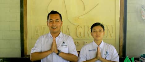 Two individuals in white uniforms standing in front of a wall with the text "AZANA GREEN RESORT".