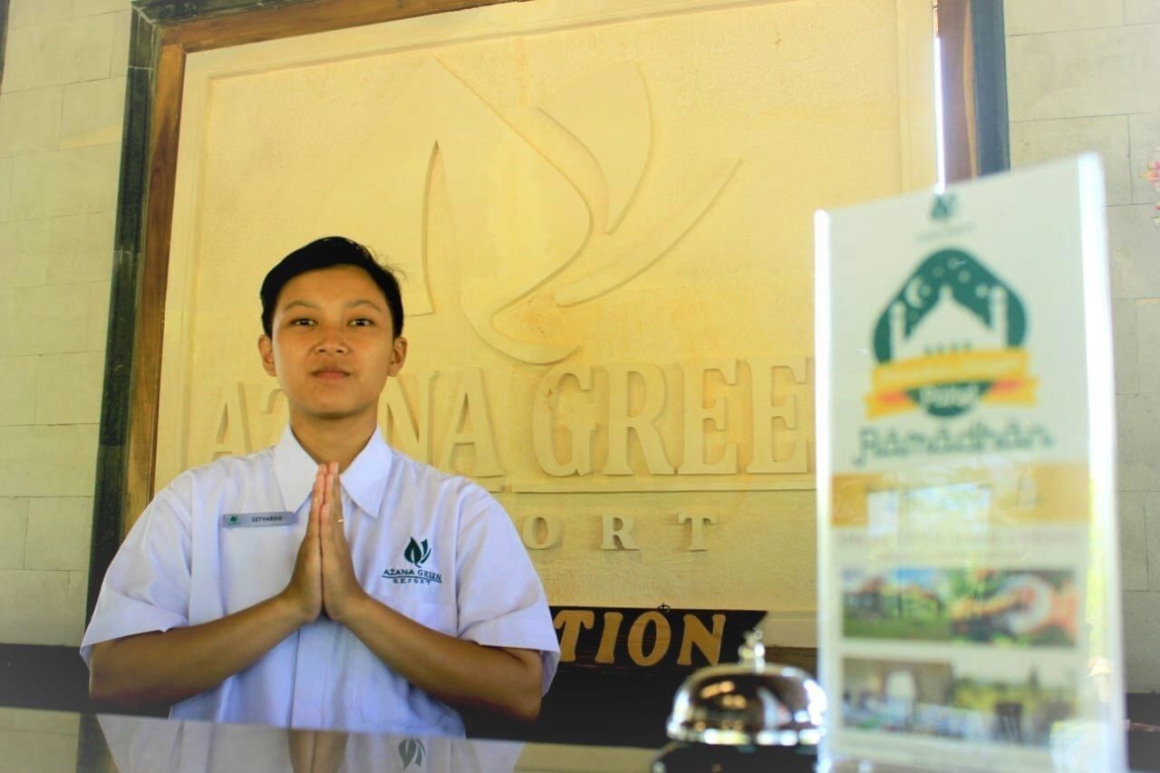 A person standing in front of a reception desk with a sign that reads "ATANA GREEL HOTEL."