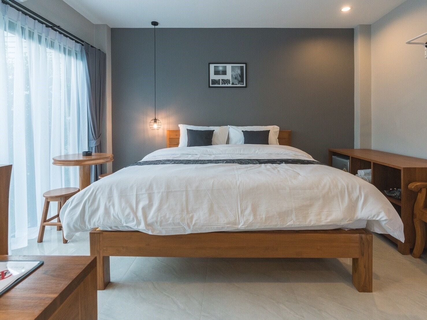 Une chambre moderne avec un lit en bois, une table de chevet, une petite table ronde et un luminaire fixé au mur.
