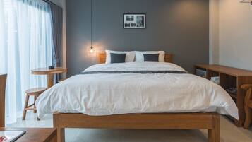Une chambre moderne avec un lit en bois, une table de chevet, une petite table ronde et un luminaire fixé au mur.