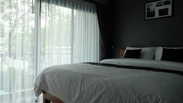 A bedroom with a large bed, white bedding, a view of trees through sheer curtains, and a framed picture on the wall.