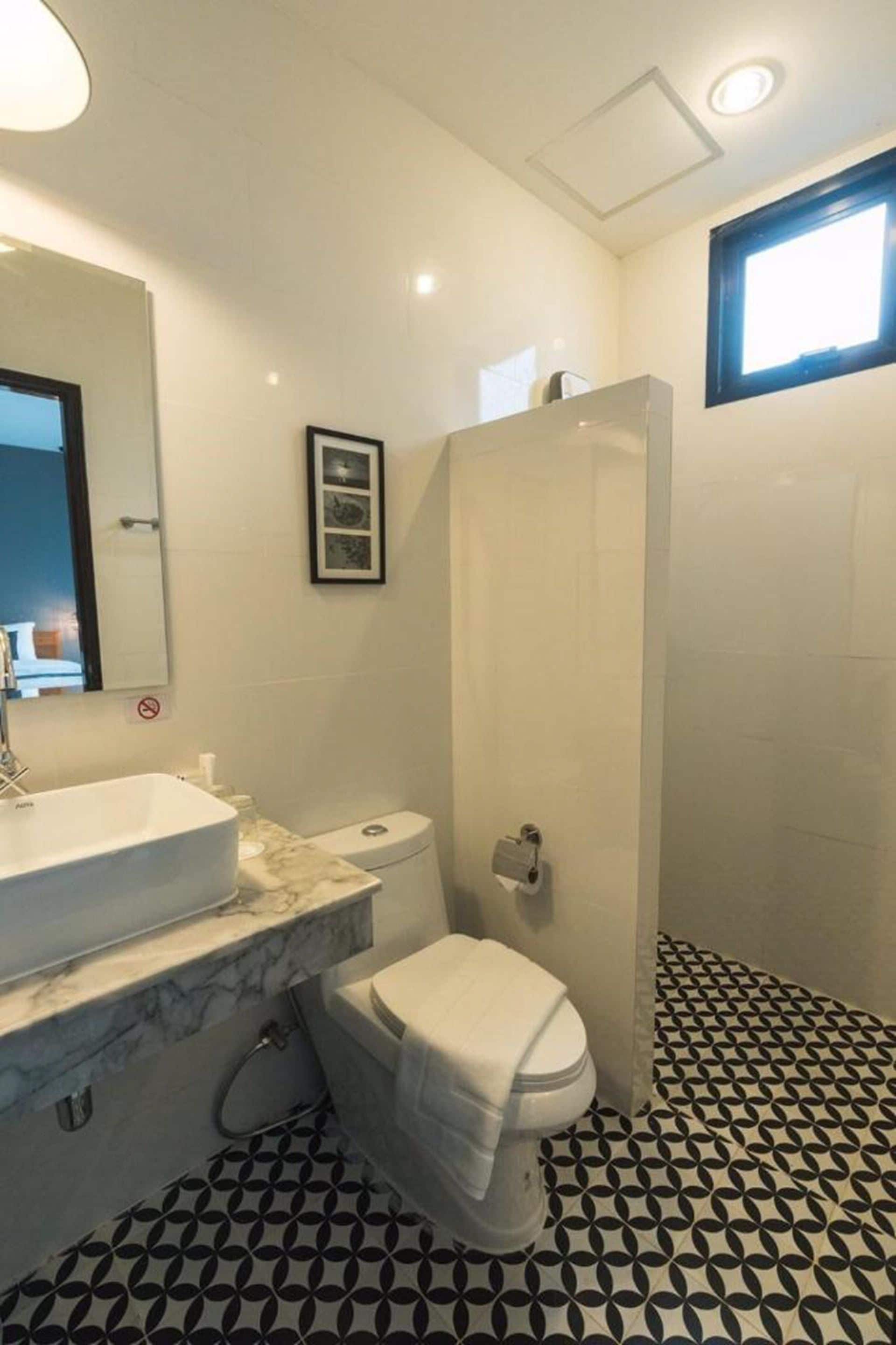 A bathroom with a white sink, toilet, and shower. The floor has a black and white geometric pattern.