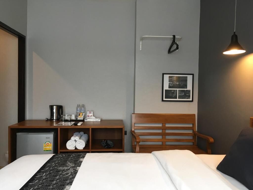 Une chambre d’hôtel avec un lit, une tête de lit en bois, un petit bureau avec une bouilloire, une machine à café et une étagère avec des serviettes.