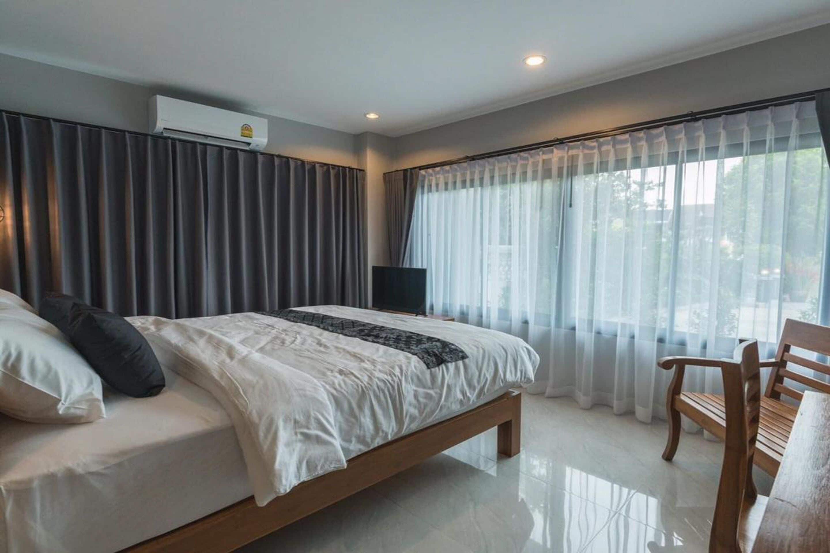 A modern bedroom with a large bed, a wooden chair, and a TV.