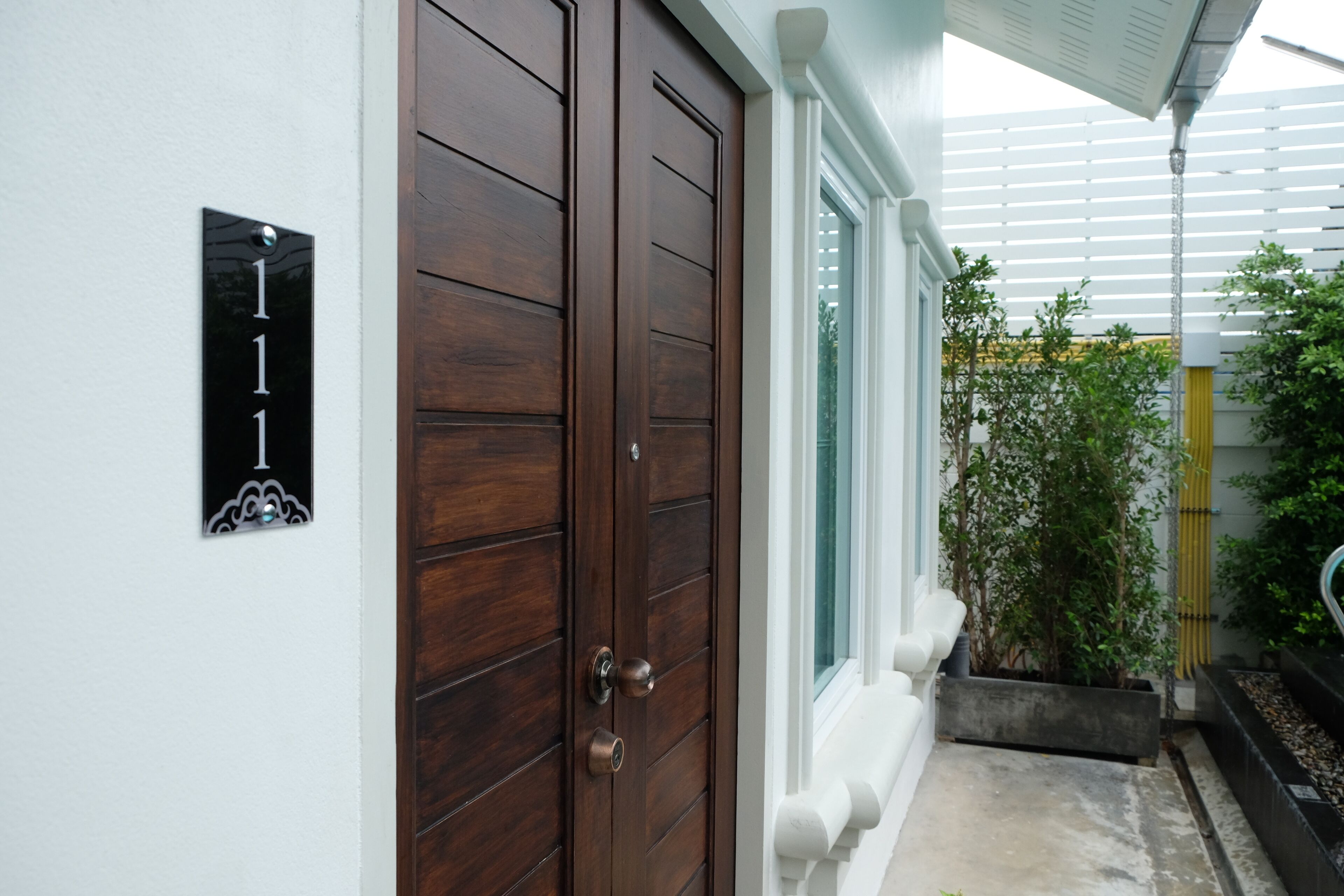 A wooden door with a number plate, a window with white shutters, and a planter with green plants.