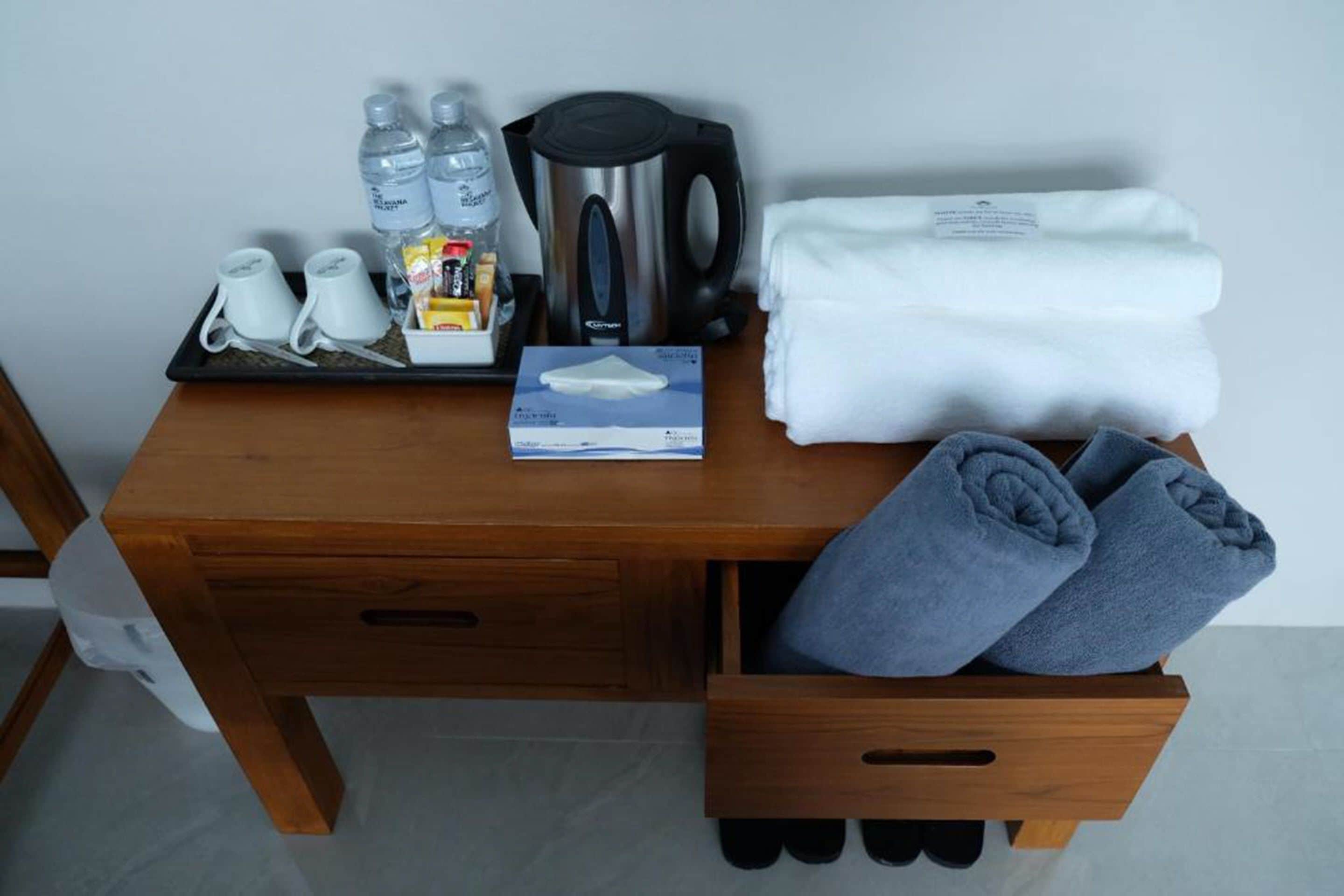 A wooden desk with a tray containing toiletries, a kettle, a box of tissues, and a folded towel.