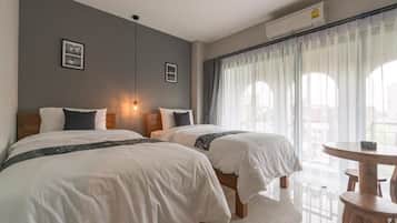 A hotel room with two beds, a round table, and a view of the outdoors through sheer curtains.