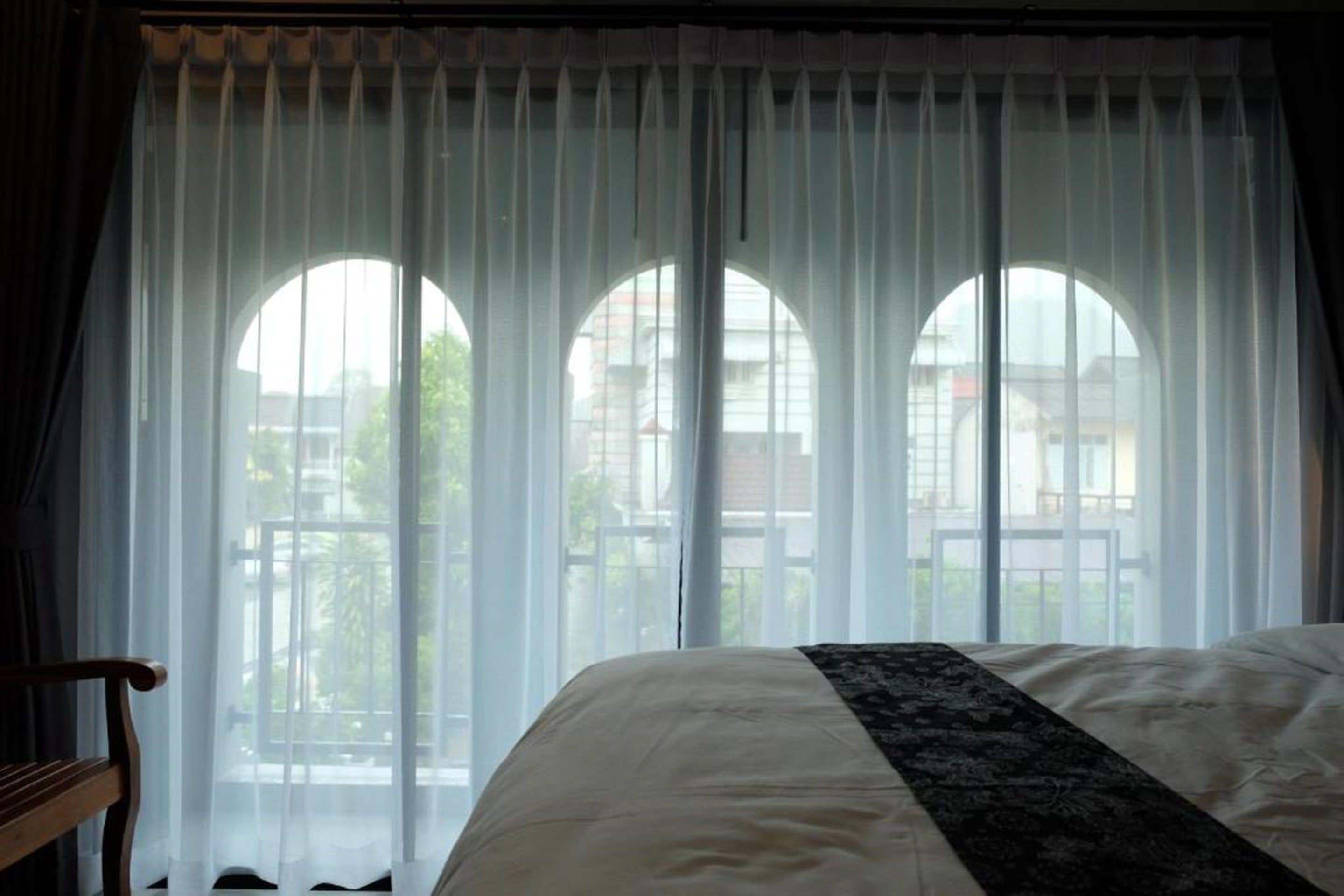 A bedroom with a bed, a wooden bench, and a window with three arched openings.