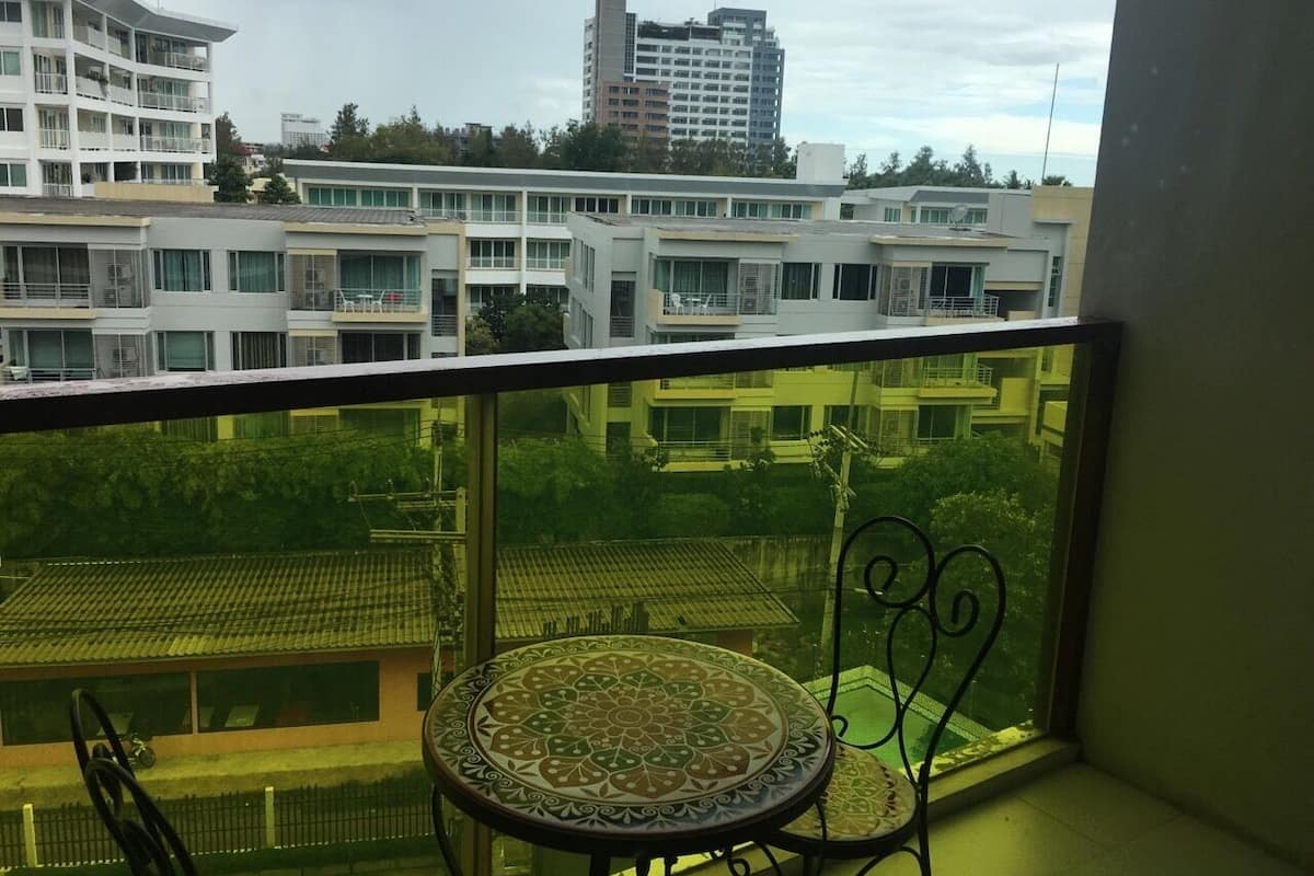 A balcony with a table and chair, overlooking a residential area with multiple buildings.