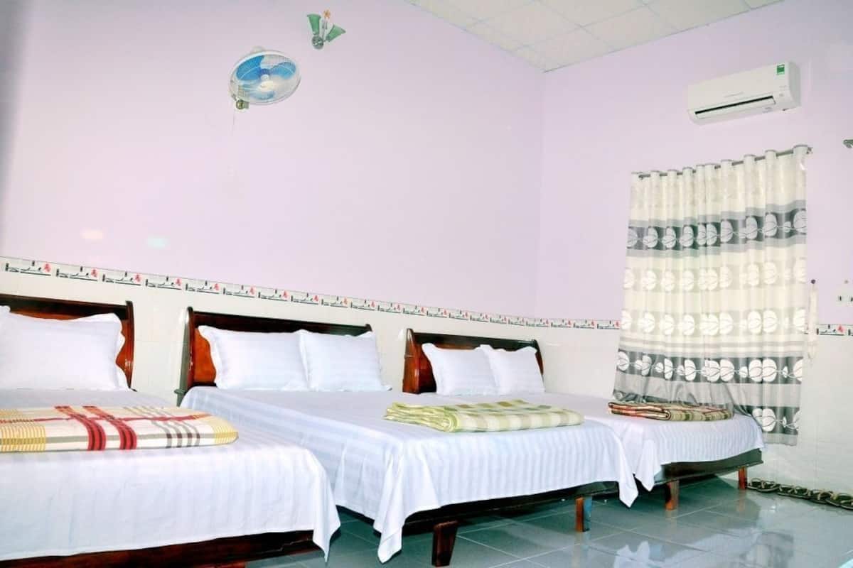 Une chambre d’hôtel avec deux lits, un ventilateur de plafond, un climatiseur et une fenêtre avec un rideau.