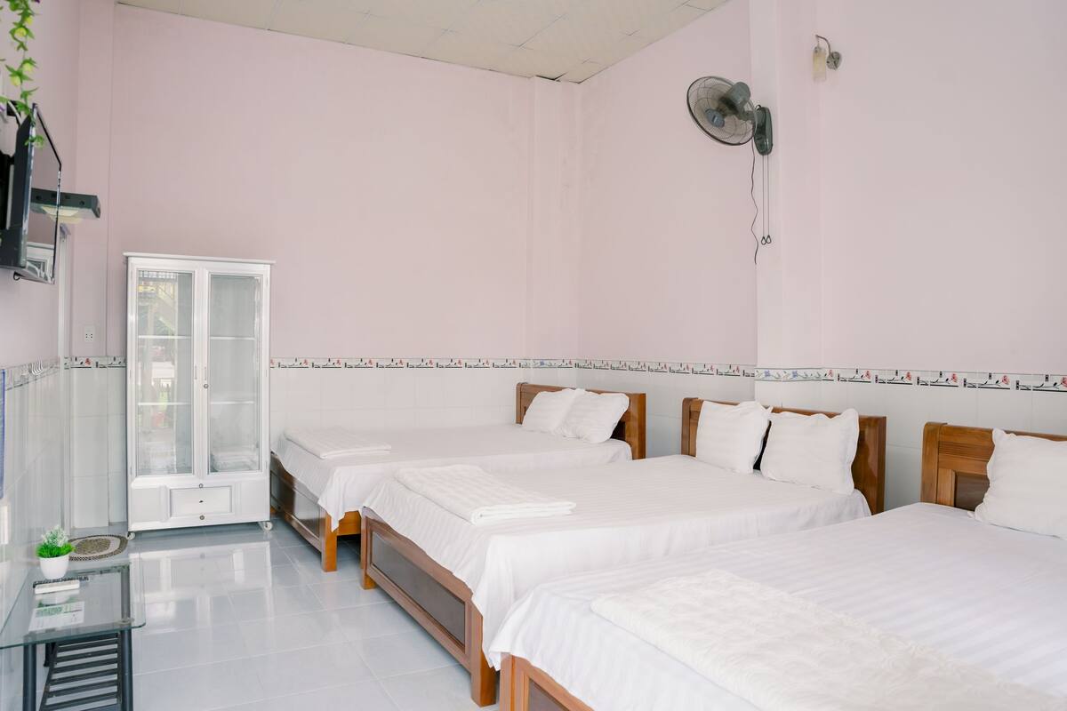 Une chambre d’hôtel avec deux lits, une petite table, une vitrine et un ventilateur fixé au mur.
